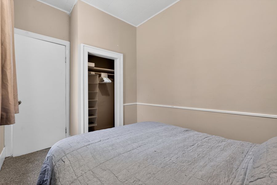 Cozy bedroom with beige walls, gray bedding, and a walk-in closet with built-in shelving.