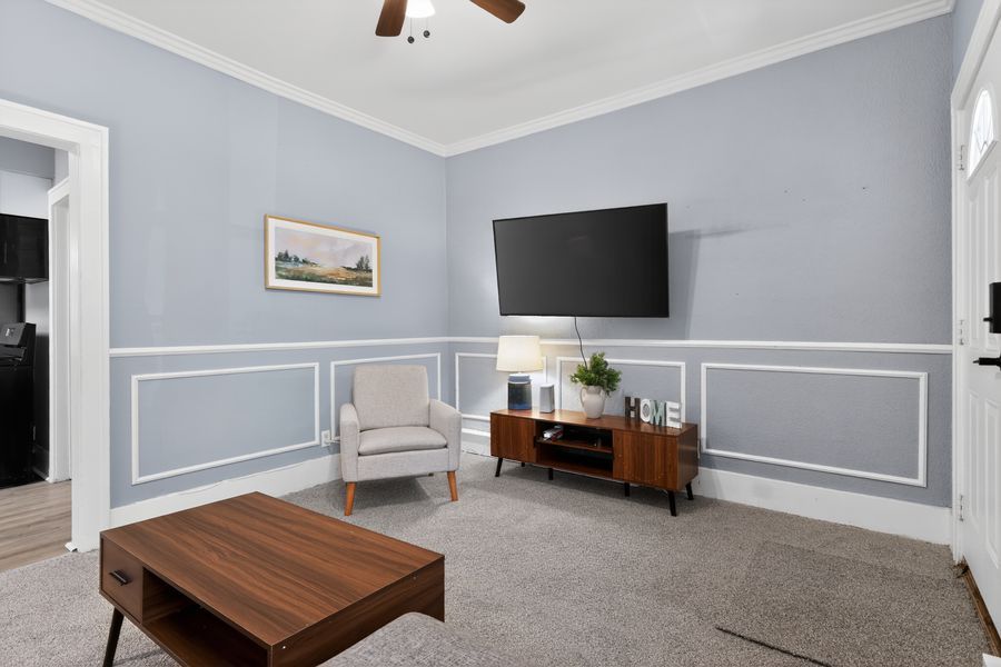 Cozy living room with light blue wainscoting walls, mounted TV, beige armchair, wood coffee table, and carpet flooring.