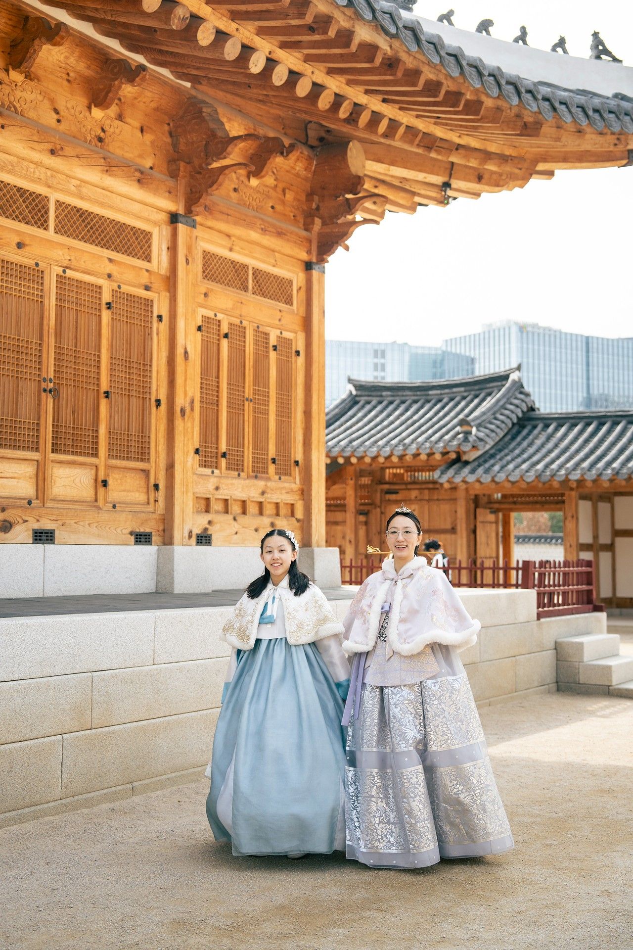 Two women wearing traditional Korean hanbok attire pose smiling at Gyeongbokgung Palace in Seoul.