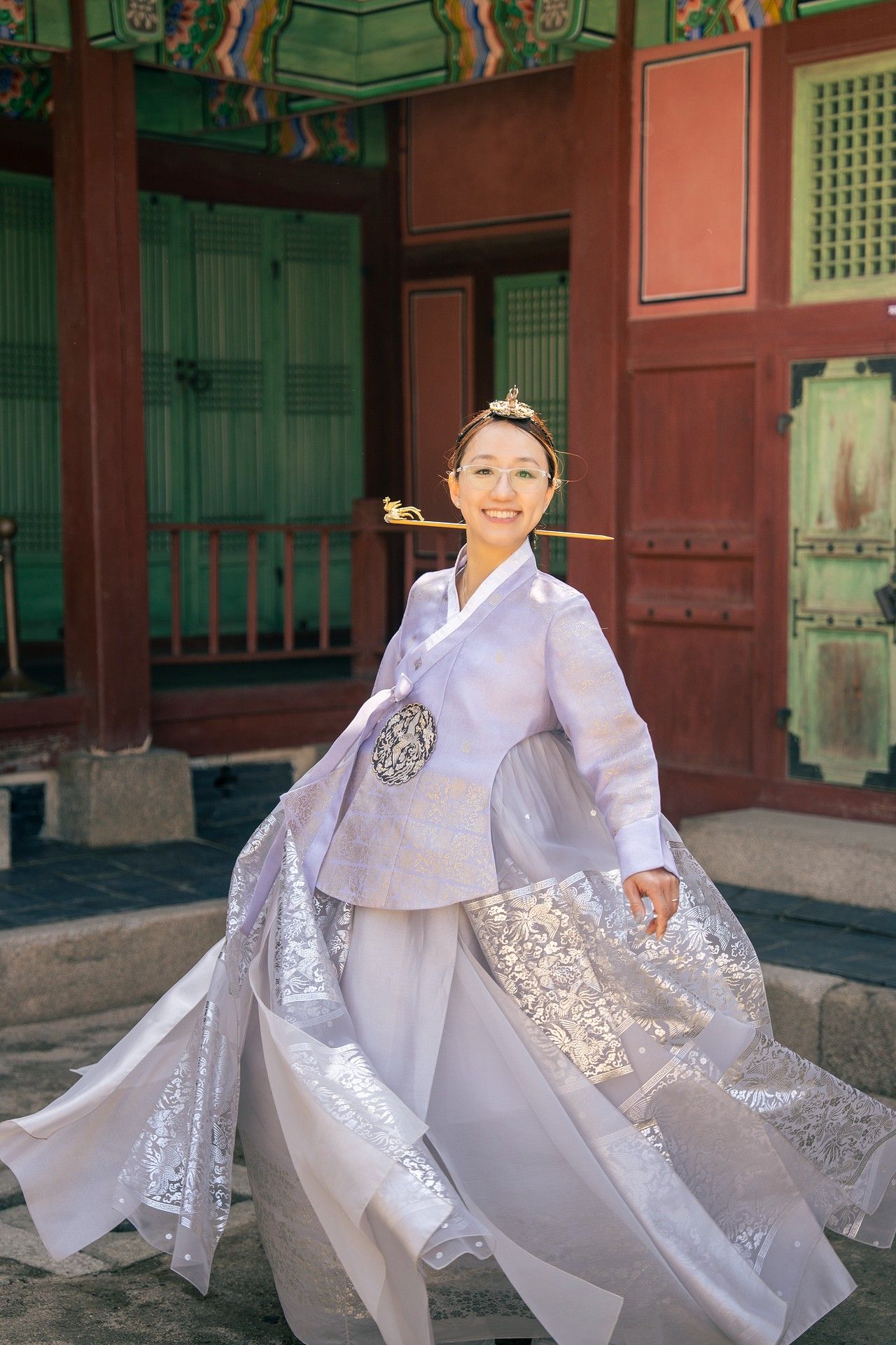 A smiling woman twirls in a white hanbok traditional Korean dress outside a historic palace building.
