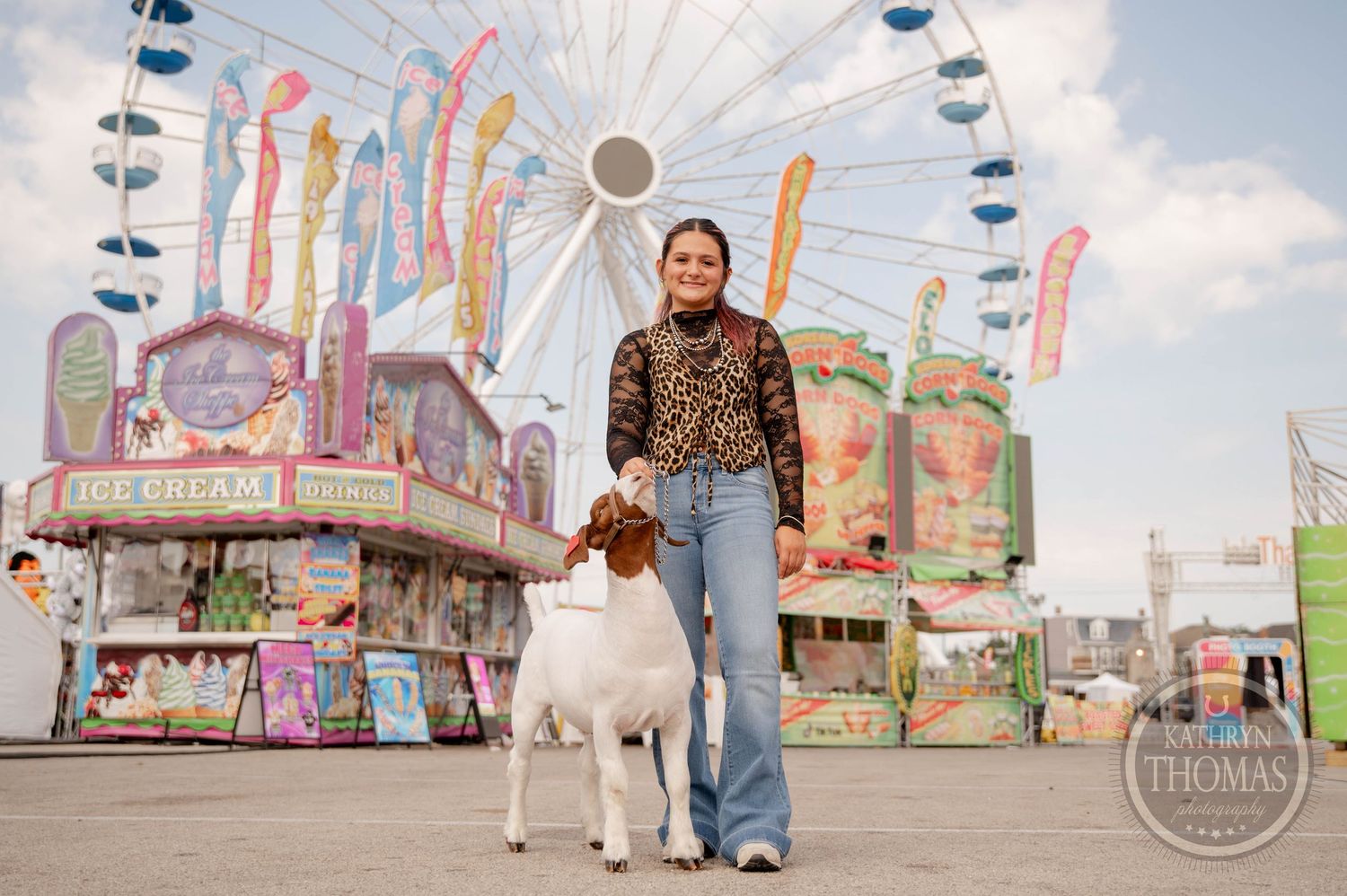 Young woman in leopard print top crouches beside a white and brown goat at a county fair.