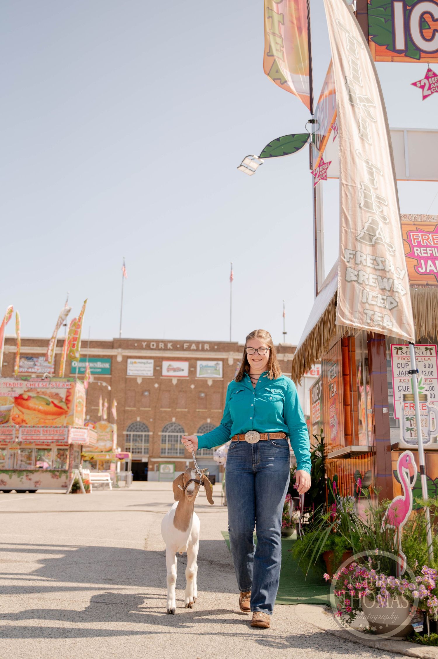 Young woman in teal shirt holds black and white cow at state fair with Ferris wheel backdrop.