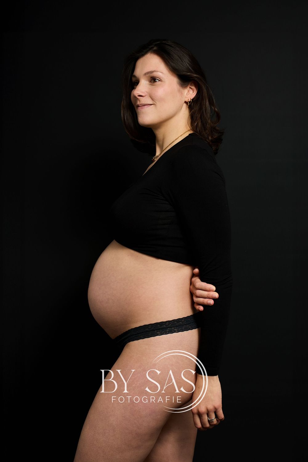 Pregnant woman in black top posing sideways, showcasing baby bump, maternity photography by BAS Fotografie.