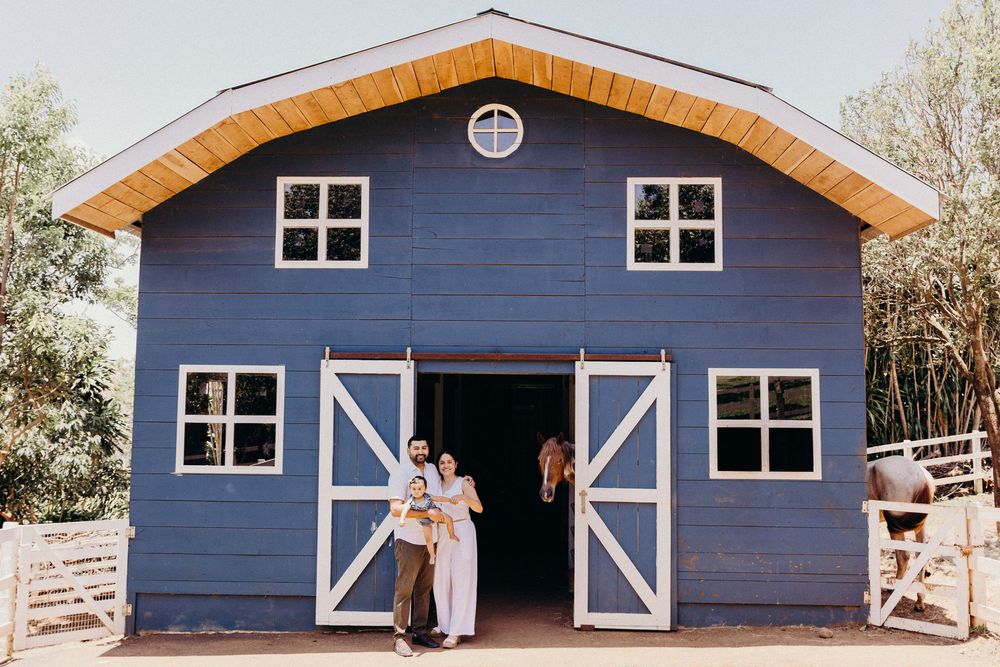 Couple standing in front of a blue barn with white sliding doors and a horse visible inside on a sunny day.