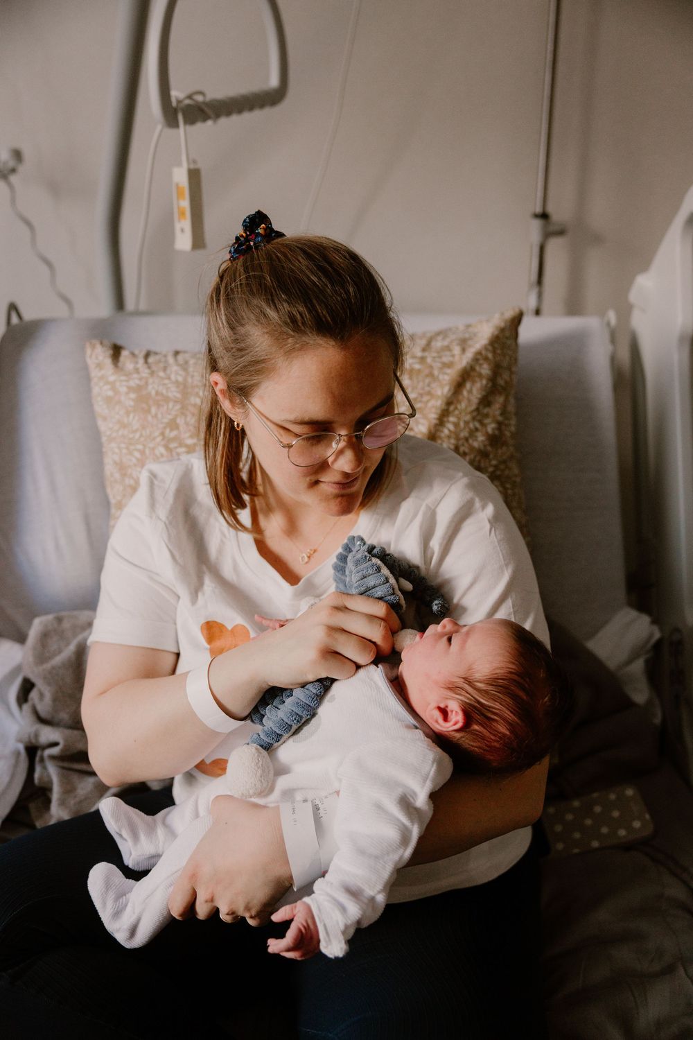New mother wearing glasses holds sleeping newborn baby in hospital room after birth.