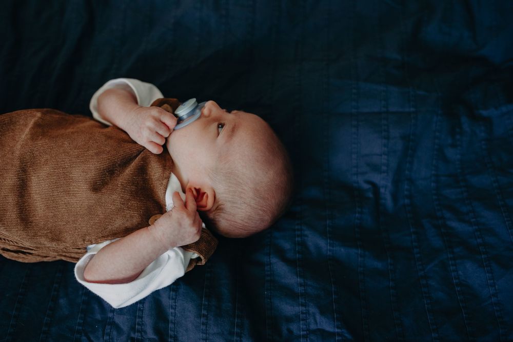 A peaceful newborn baby lying on a dark blue linen blanket with a pacifier.