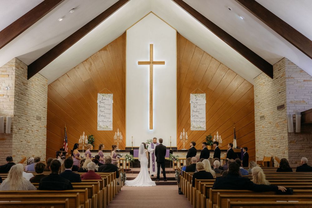 Elegant church wedding ceremony with couple at altar beneath wooden cross, guests seated in pews, warm candlelit ambiance.