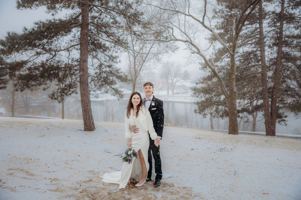 Bride and groom pose together in a snowy winter landscape surrounded by tall trees during their outdoor wedding.