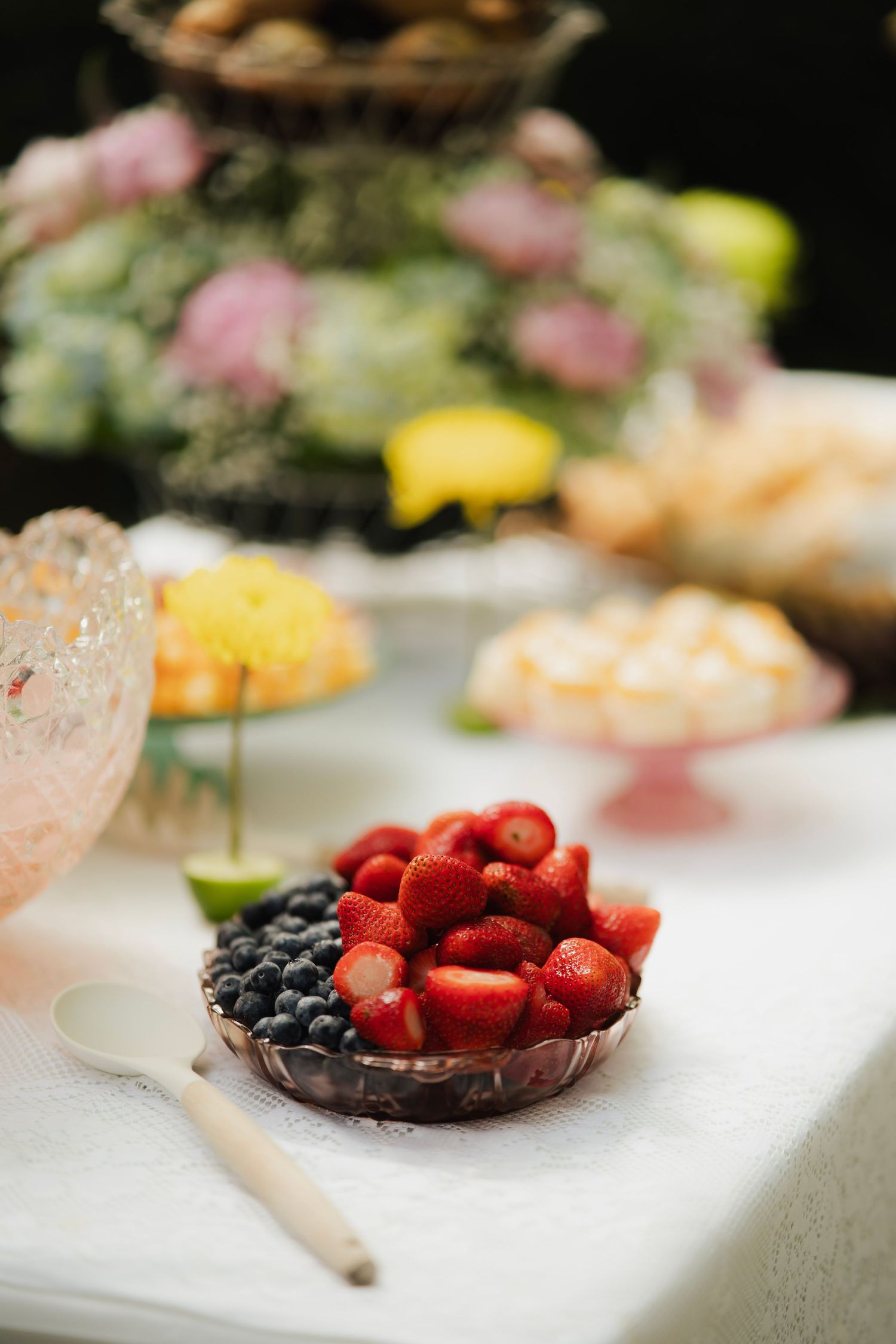 Bowl of fresh strawberries and blueberries on white tablecloth at an outdoor garden party dessert table.