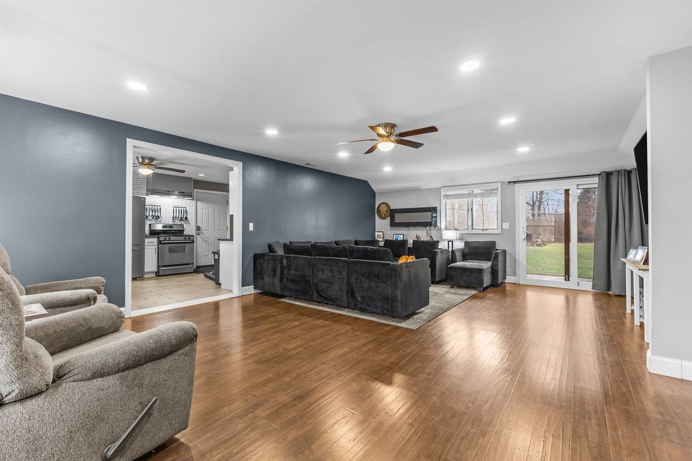 Spacious living room with hardwood floors, blue accent wall, ceiling fan, recessed lighting, and sliding glass door to backyard.