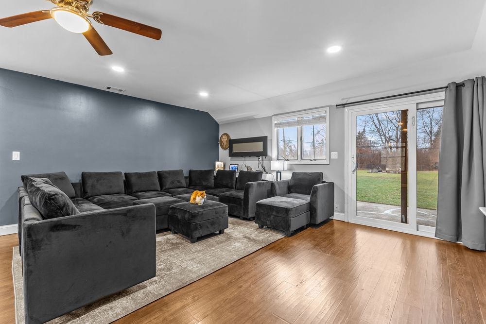 Modern living room featuring large gray sectional sofa, hardwood floors, ceiling fan, and sliding glass doors to backyard.