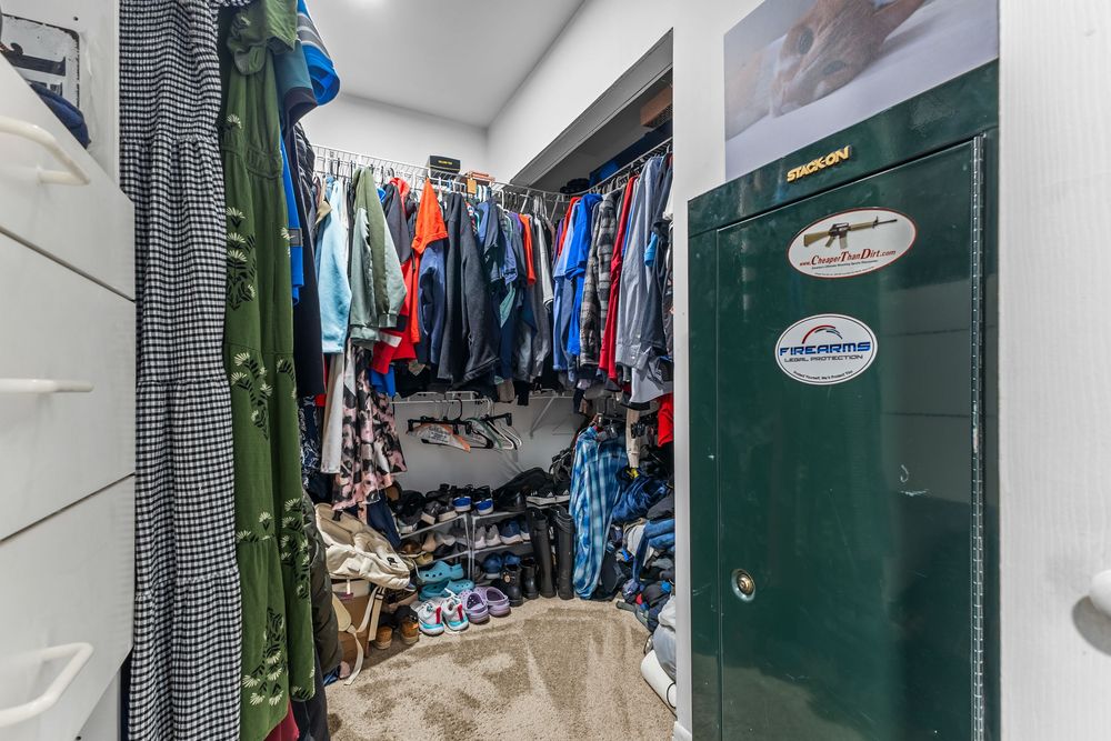 Cluttered walk-in closet with packed clothing rods and a green gun safe beside the entrance door.