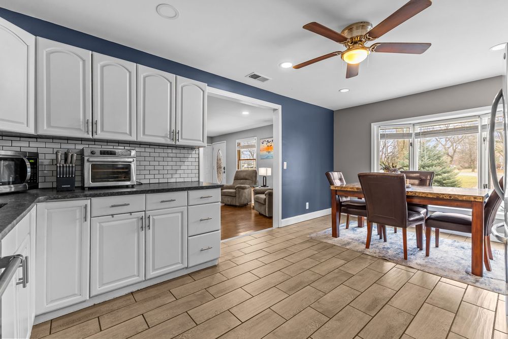 Bright kitchen with white cabinets, subway tile backsplash, and open view to dining area with wood table.