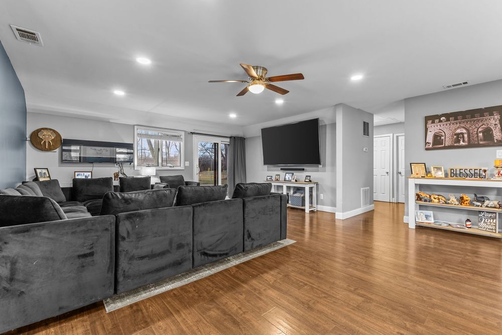 Spacious living room with gray sectional sofa, hardwood floors, ceiling fan, wall-mounted TV, and recessed lighting.