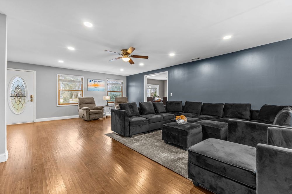 Spacious living room with dark sectional sofa, hardwood floors, ceiling fan, and accent blue wall with recessed lighting.