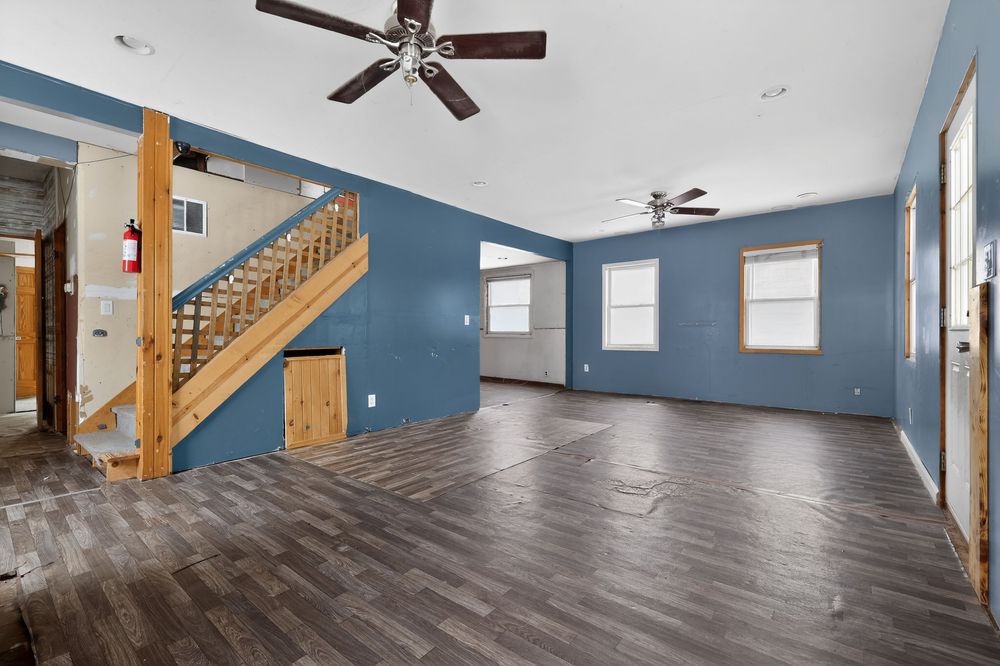 Spacious living room with blue walls, dark hardwood floors, wooden staircase, and ceiling fans.
