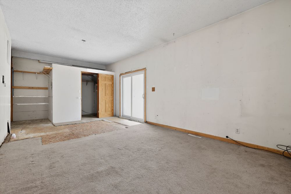 Empty room with carpet flooring, sliding closet doors, and textured ceiling in a home undergoing renovation.
