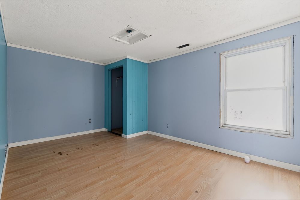 Empty room with blue walls, light wood floors, white trim, and a single window allowing natural light.