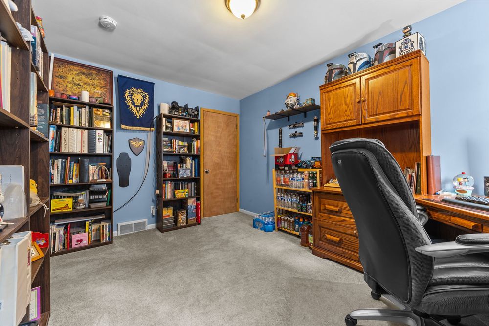 Home office with blue walls, bookshelf, wooden cabinet, black leather chair, and carpet flooring.