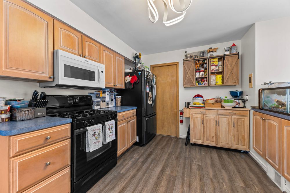 Modern kitchen with light wood cabinets, black appliances, hardwood floors, and a barn door pantry.