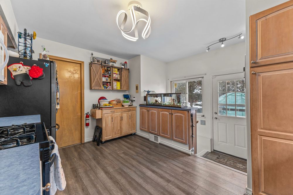 Kitchen with wood cabinets, hardwood floors, modern chandelier, and a bright door leading to an exterior entrance.