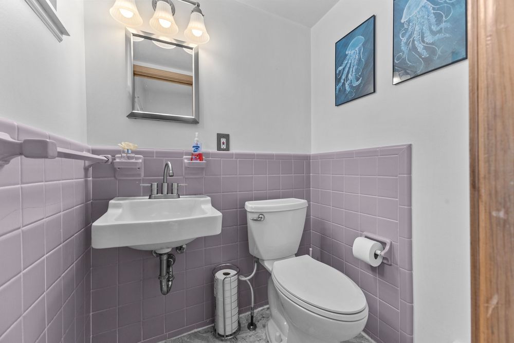 Half bathroom with purple tile wainscoting, wall-mounted sink, white toilet, and decorative ocean art on white walls.