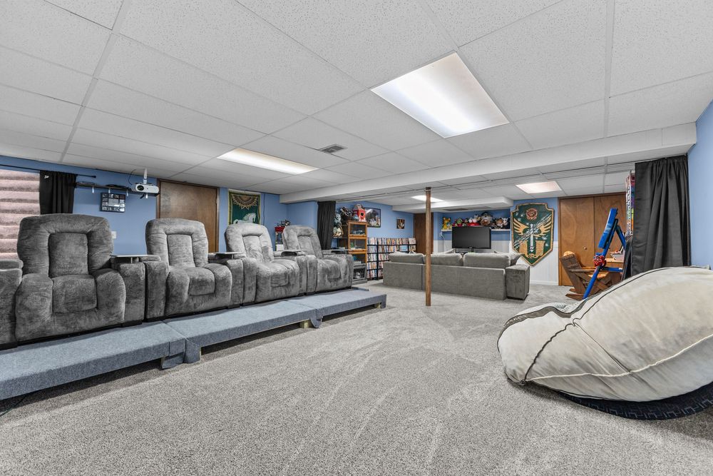 Spacious basement home theater with recliner seating, bean bag chair, carpeted floors, and drop ceiling with recessed lighting.