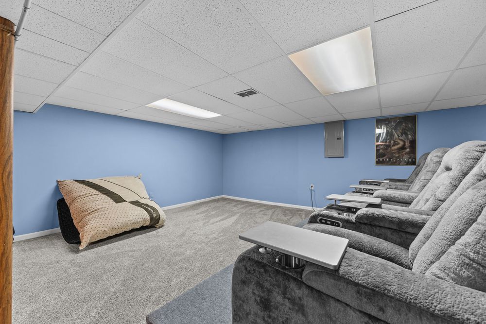Basement home theater room with recliner seating, blue walls, drop ceiling, and carpet flooring.