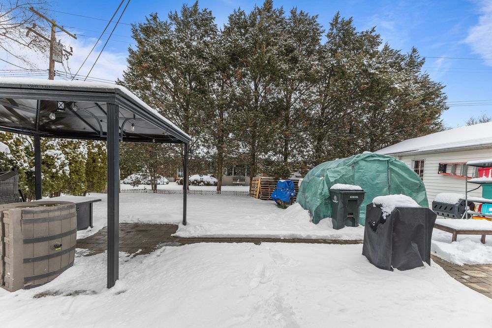 Snow-covered backyard with pergola, BBQ grill, and green tent storage in a residential property during winter.