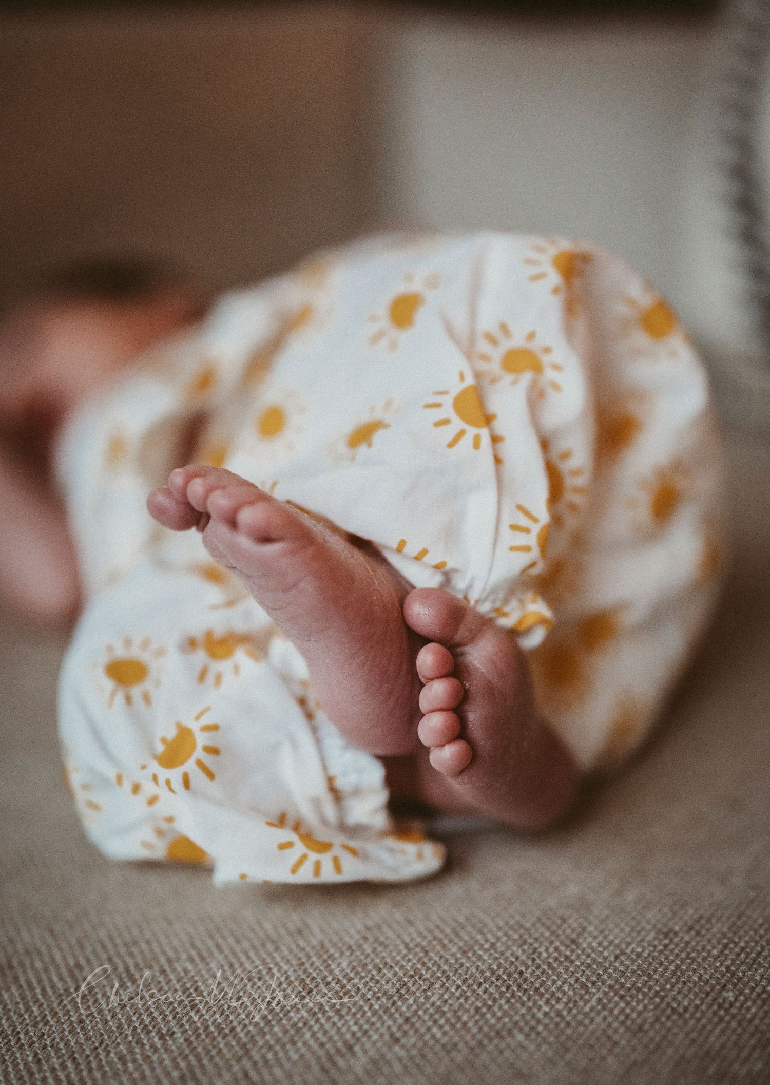 Close-up of newborn baby feet peeking out from a white swaddle blanket with yellow sunshine print pattern.