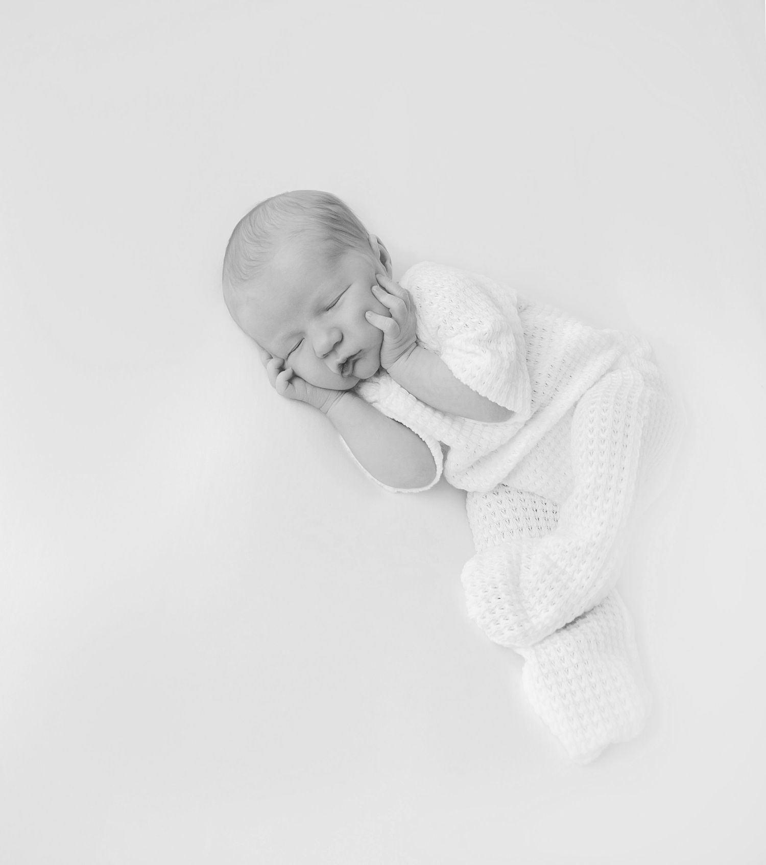 Newborn baby lying on white blanket wrapped in pink, looking at the camera.