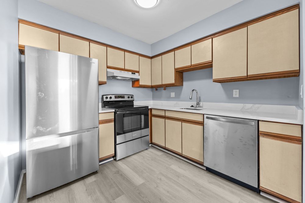 Modern kitchen featuring stainless steel appliances, light wood cabinetry, and hardwood floors.