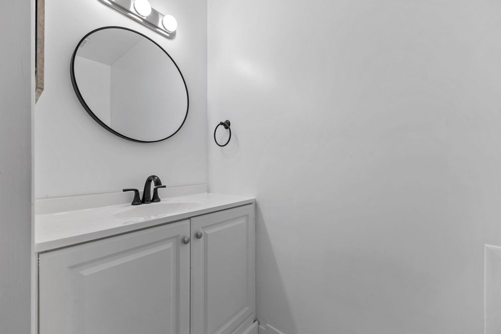Clean white bathroom vanity with round black-framed mirror and modern black fixtures.