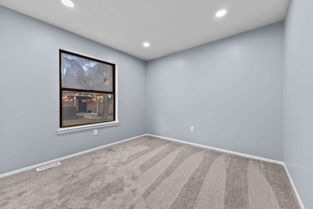 Empty bedroom with gray carpet, recessed lighting, and large window with outdoor view.