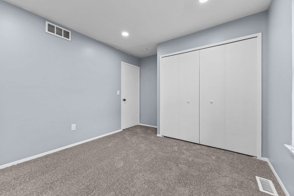 Carpeted bedroom with white bi-fold closet doors and recessed lighting in gray-walled room.