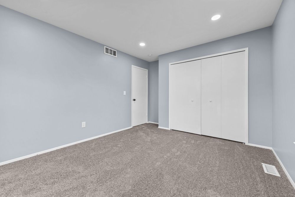 Neutral carpeted bedroom with white closet doors, recessed lighting, and light gray walls.