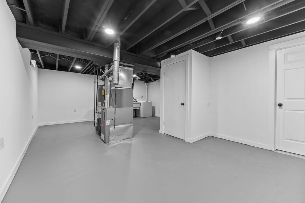 Unfinished basement utility area with exposed black ceiling joists, HVAC equipment, and gray epoxy floors.