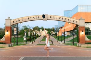 Graduate poses gracefully beneath the iconic Kent State University arch at golden hour on campus.