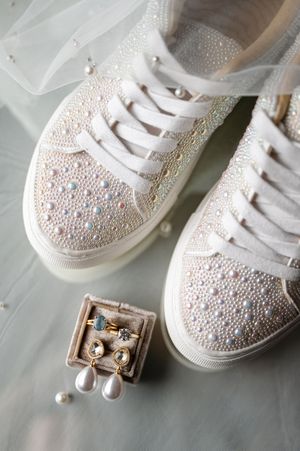Pearl-embellished white bridal sneakers with matching jewelry box containing gold drop earrings on soft blue background.