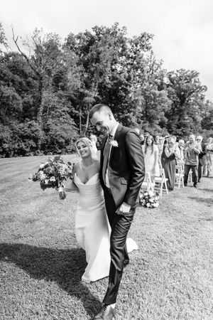 Black and white photo of a joyful bride and groom walking down the aisle after their outdoor wedding ceremony.