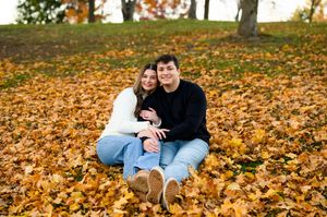 Couple sitting in autumn leaves smiling during fall engagement photo session.