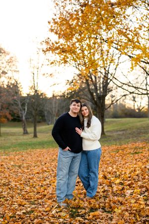 Couple embracing in a park covered with golden autumn leaves beneath colorful fall foliage trees.