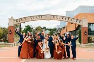 Wedding party celebrating under the Kent State University arch in rust and navy attire.