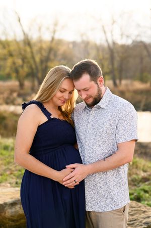 Expecting couple tenderly embracing outdoors during golden hour maternity photo session near a creek.