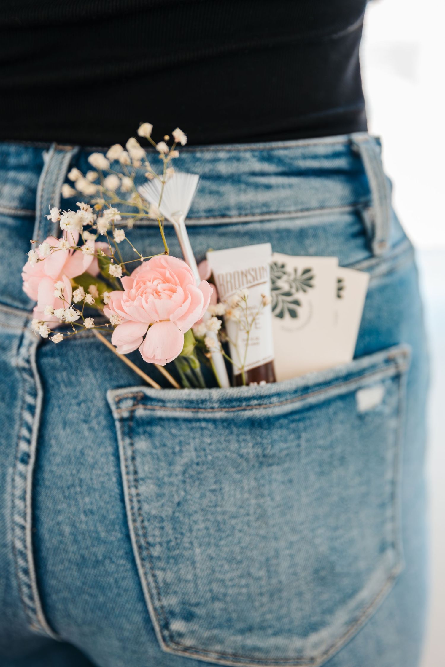 Pink roses and baby's breath tucked into the back pocket of blue denim jeans with small cards. spa salon branding pictures. fun headshots