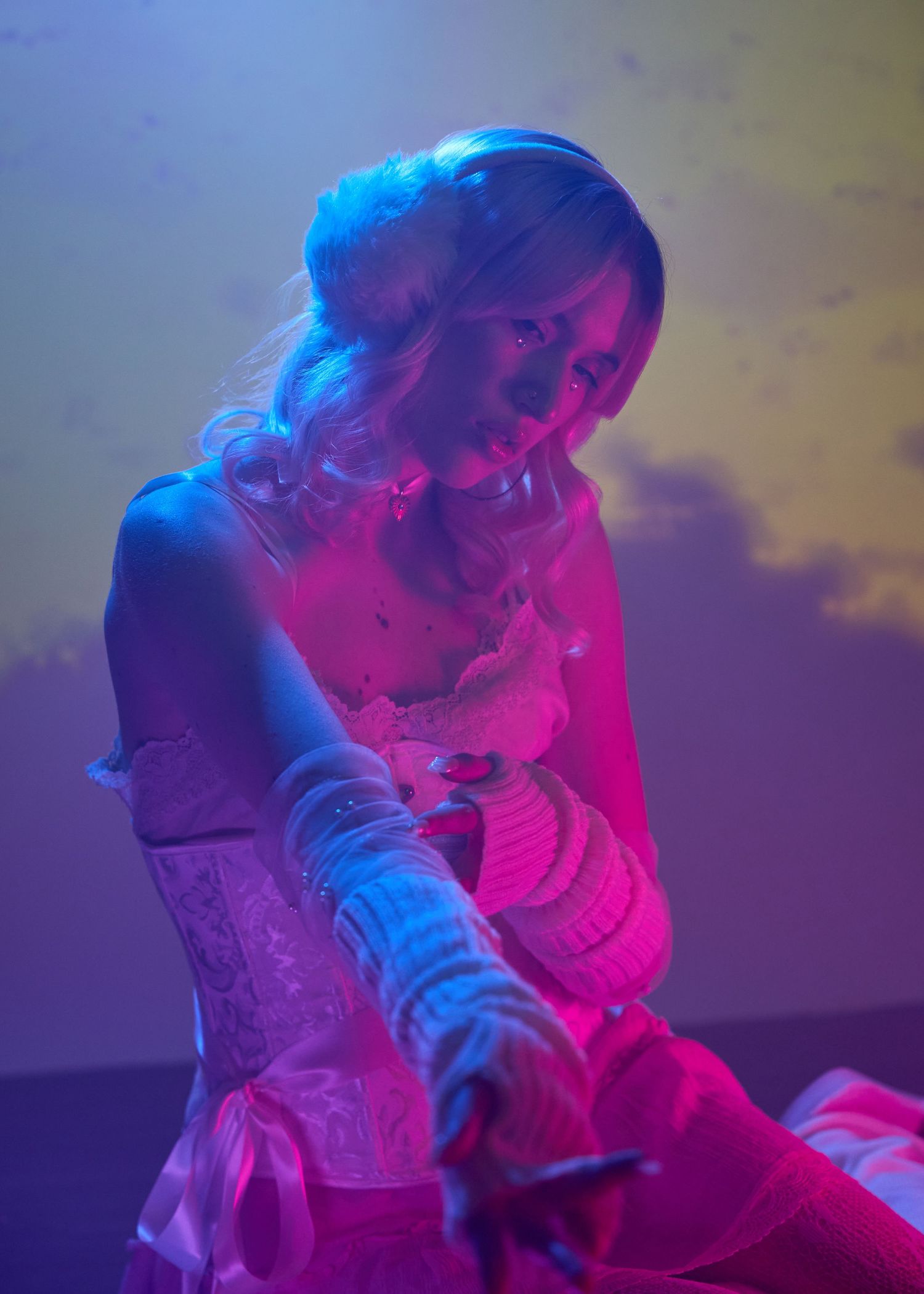 Woman in pink lace dress and white gloves poses under vibrant blue and pink neon stage lighting.