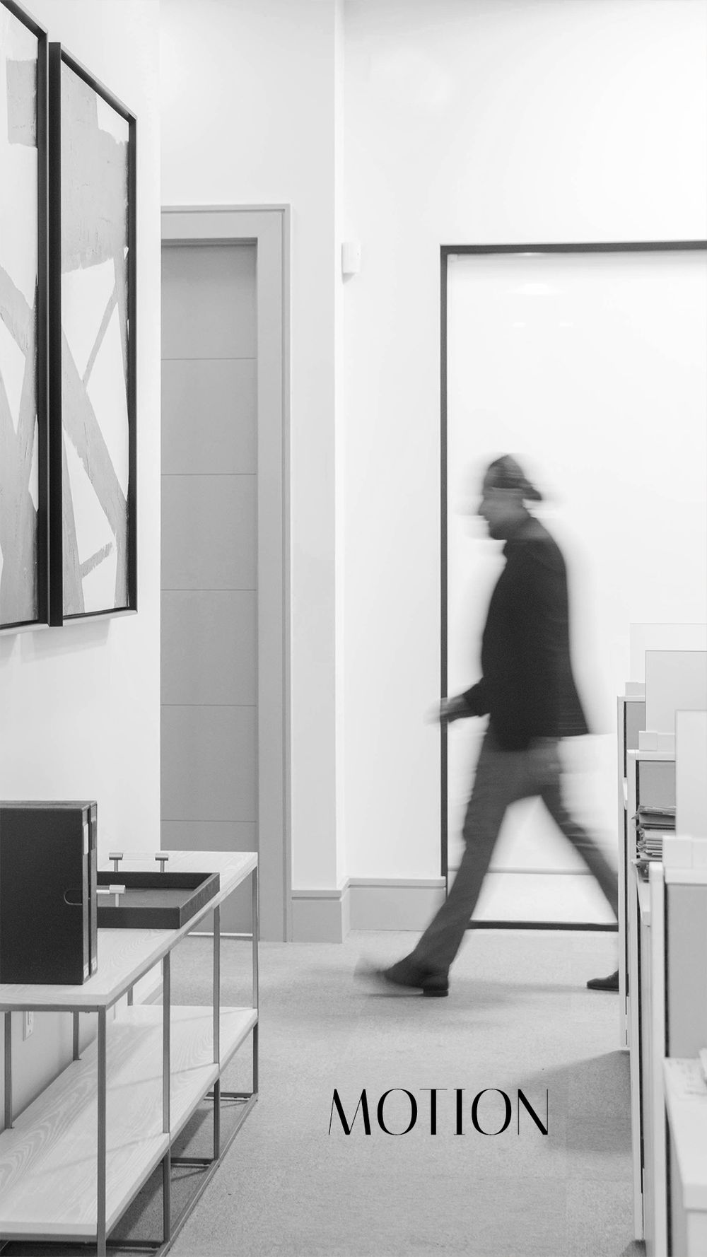 Blurred figure of a man walking through a modern minimalist gallery space in black and white motion photography.