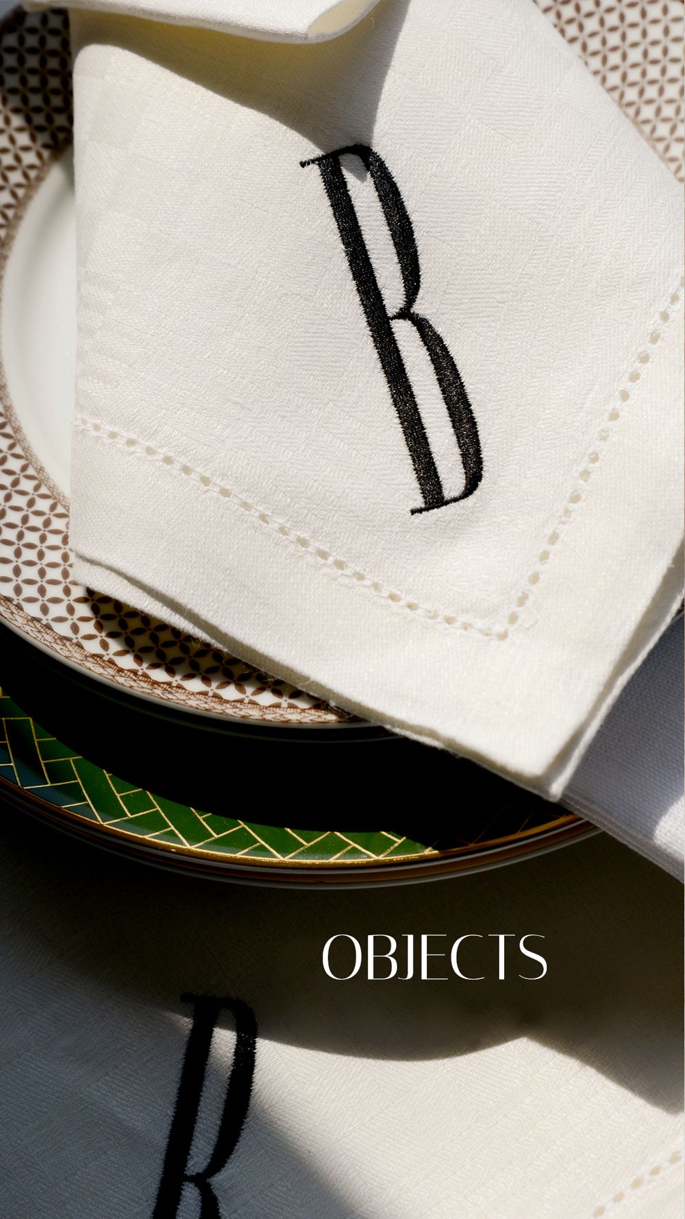White linen napkin with embroidered letter B monogram resting on decorative green and gold plates.