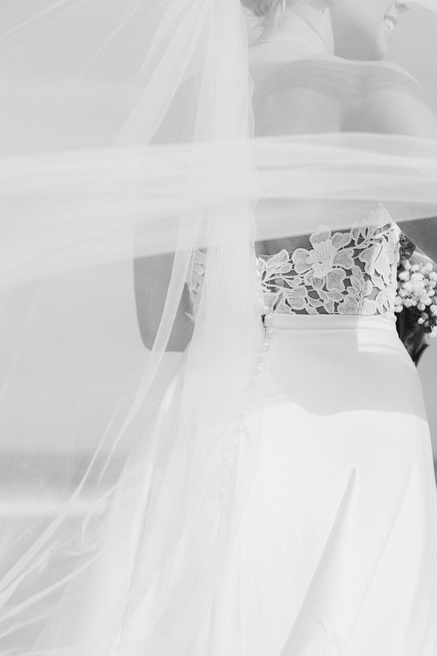 Black and white photo of a bride in lace wedding dress partially covered by flowing veil fabric.