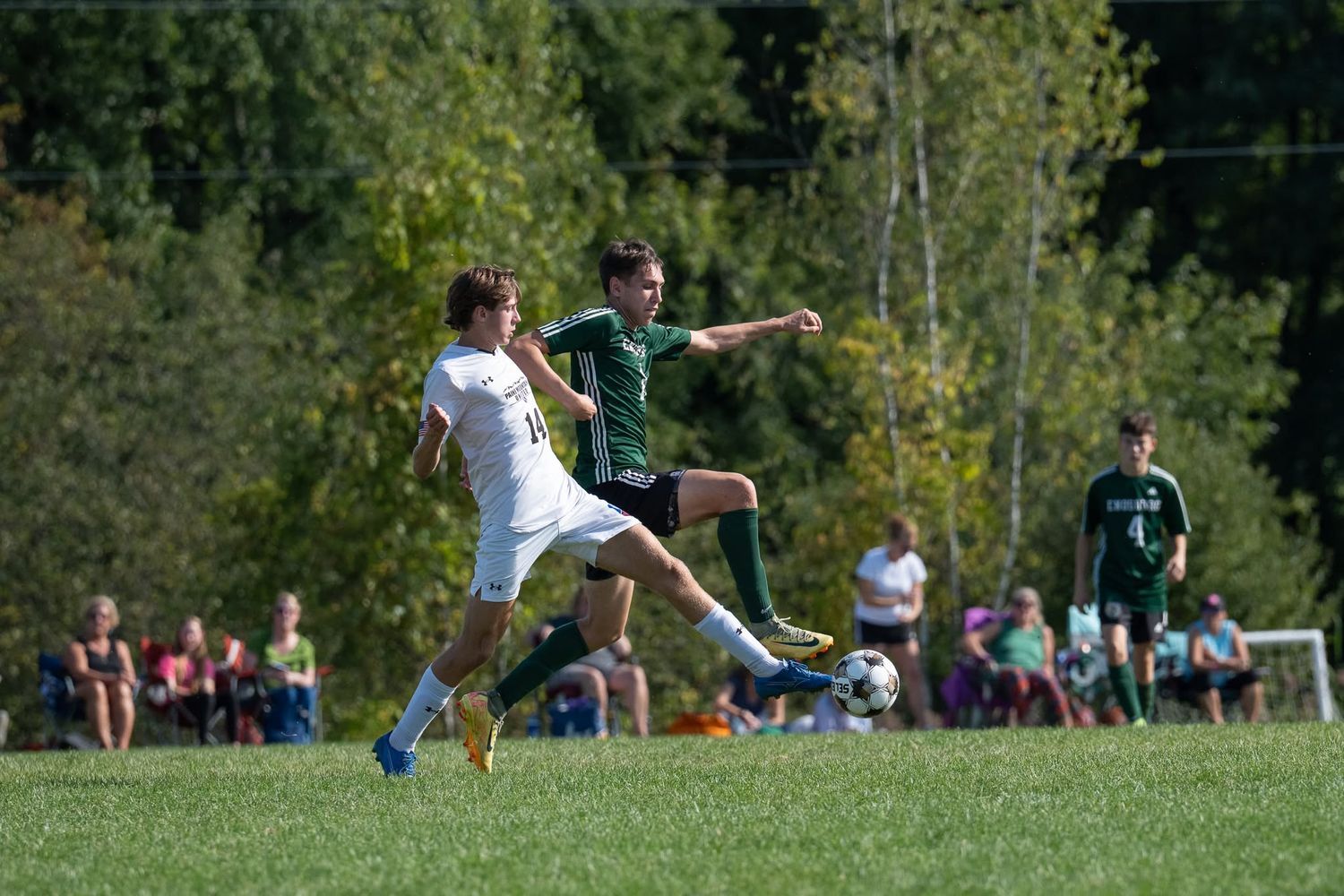Two male soccer players battle for ball during sunny outdoor high school soccer match.